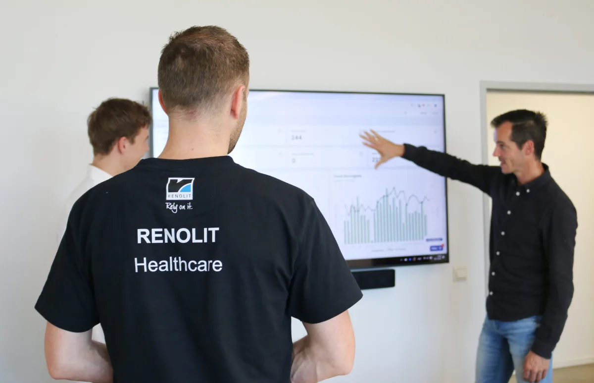BA Drie mensen bespreken een onderhoudsdashboard op een groot scherm bij RENOLIT Healthcare